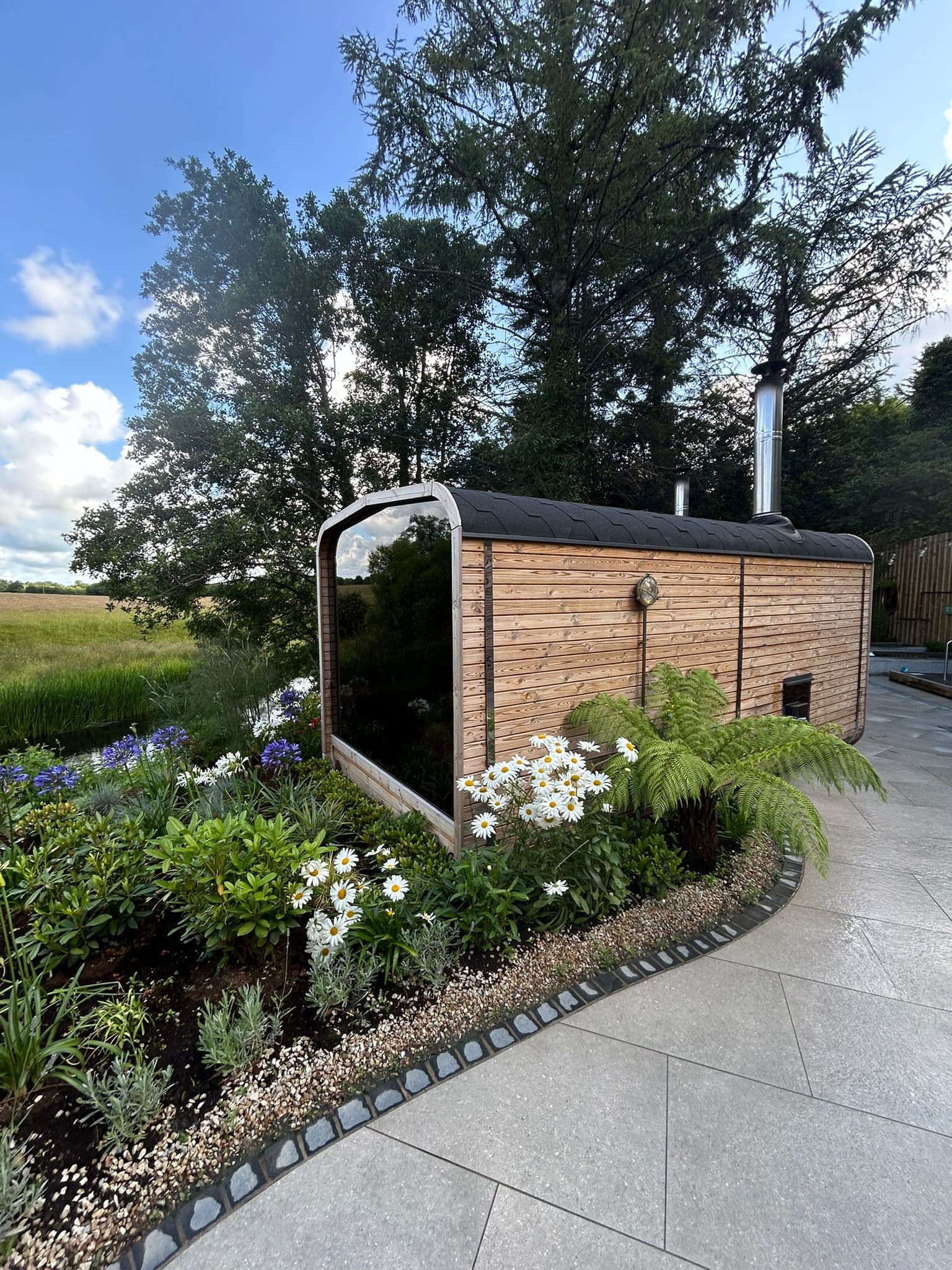 A Northern Ritual outdoor sauna cabin surrounded by ferns, wildflowers and mature trees.